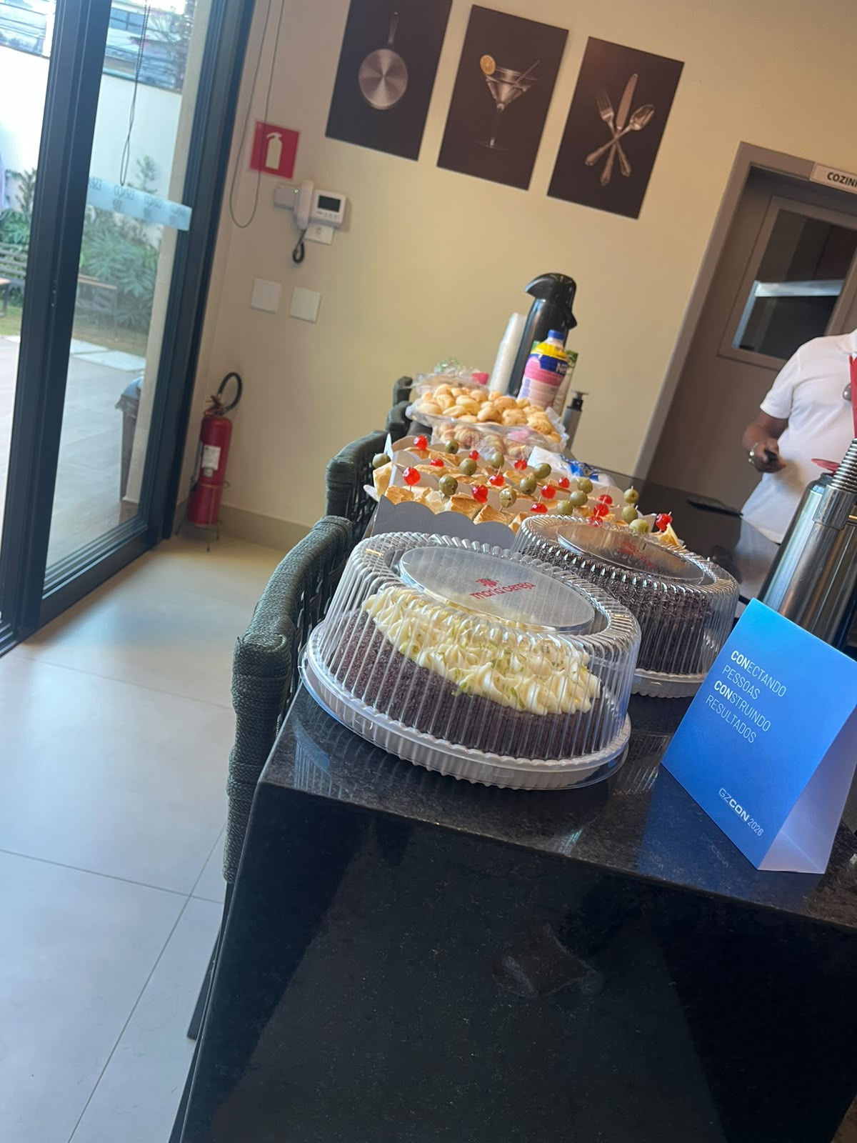 Coffee break de evento corporativo com bolos, salgados e sinalização do evento