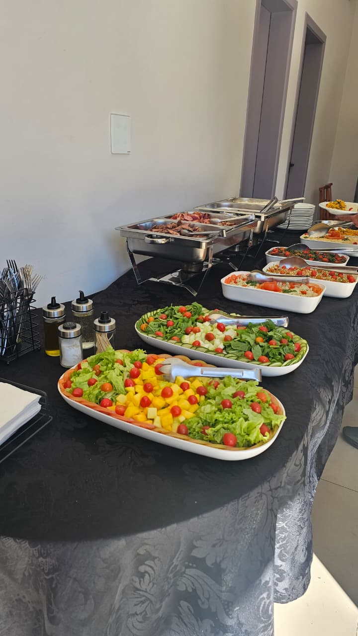 Buffet corporativo servido em mesa com saladas, grelhados e réchauds